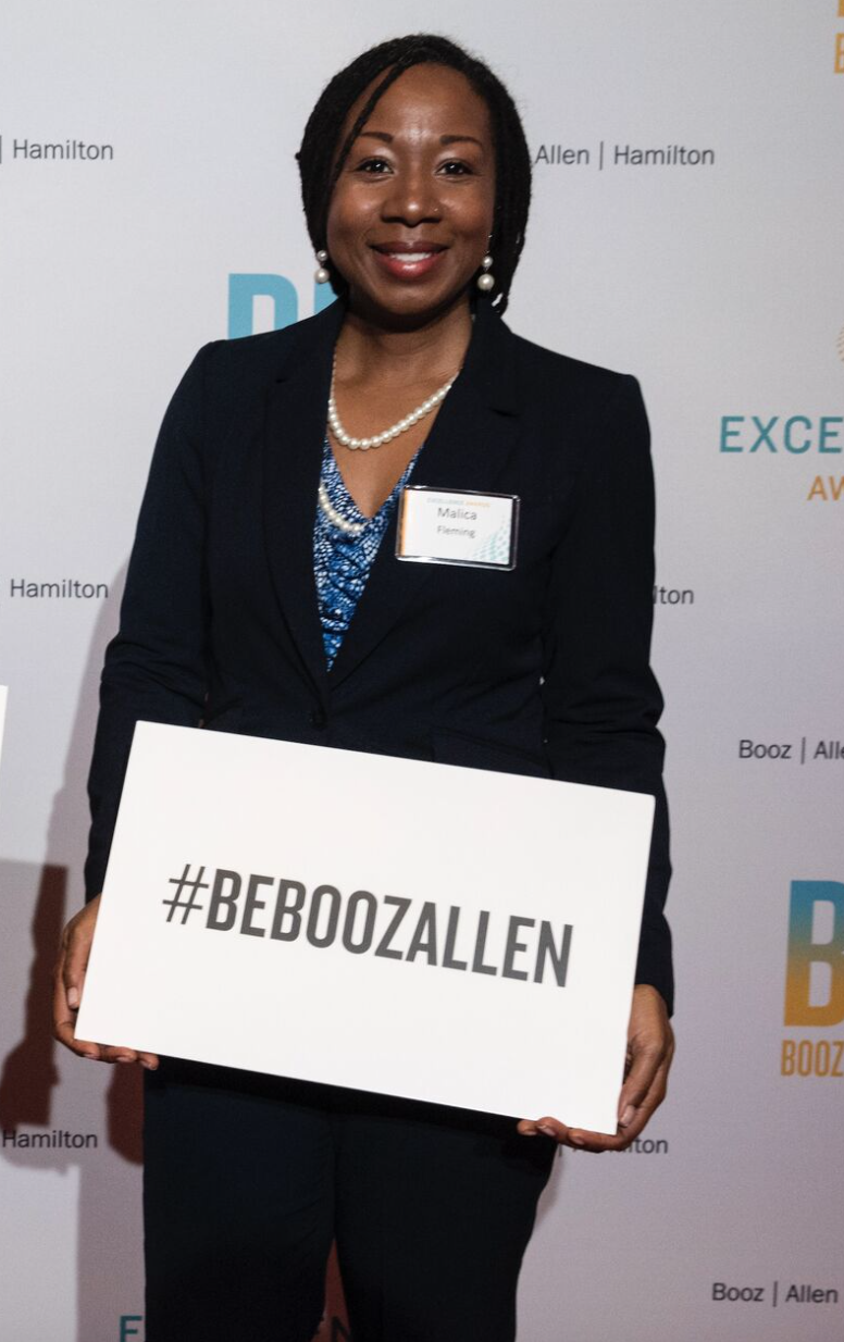 Malica Ahmad at a Booz Allen Hamilton event holding a #BEBOOZALLEN sign